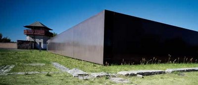 Rostiger Stahlcontainer als modernes Architekturprojekt auf dem historischen Gelände des KZ-Gedenkstatts Oranienburg-Sachsenhausen unter blauem Himmel mit altem Wachturm im Hintergrund