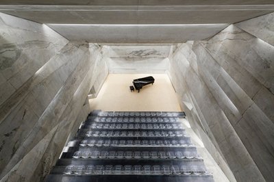 Blick von oben auf eine Treppe in einem monumentalen Betonbau mit Klavier im Hintergrund.